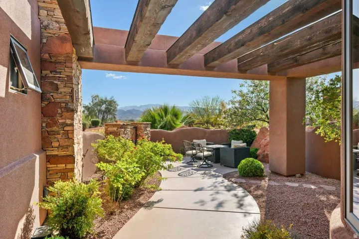 Covered patio with exposed wood beams, stone accent column, concrete pathway, and gravel landscaping