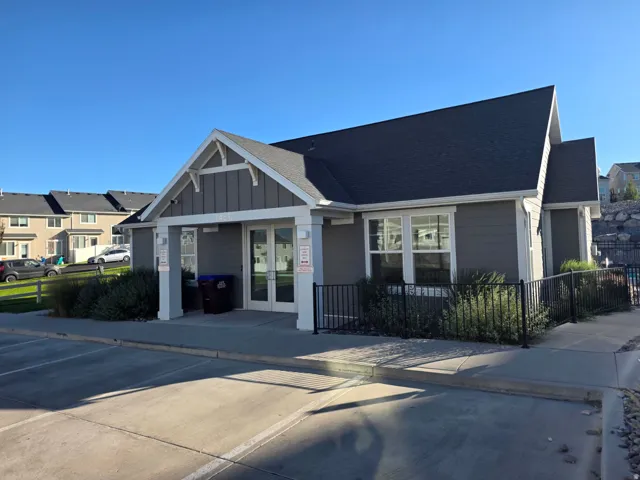 Single-story clubhouse featuring a gabled roofline, gray siding, white trim, and a black metal fence
