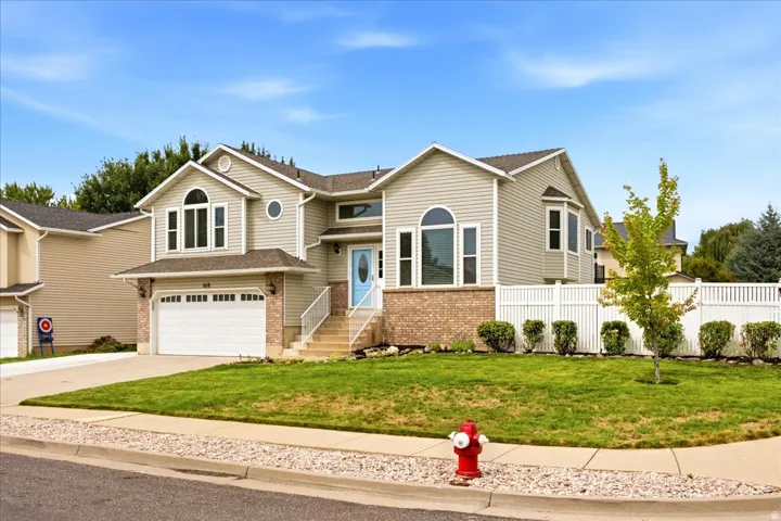 Multi-level residence featuring light-toned siding, a two-car garage, an arched picture window, and a light blue front door