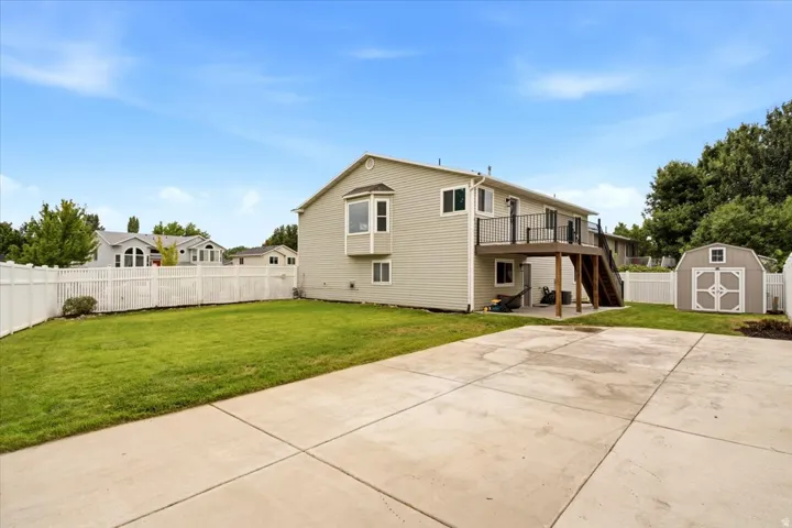 Expansive concrete patio with a green lawn, white vinyl fence, and a storage shed