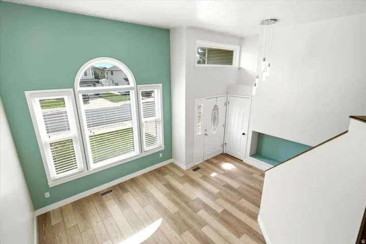 Vaulted ceiling with a contemporary chandelier, wood-finish flooring, arched window with white blinds, white entry door with decorative glass, and a built-in storage niche
