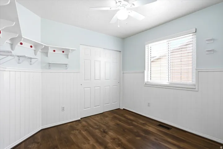 Wood-finish flooring, white paneled wainscoting, white window blinds, and a ceiling fan with integrated lighting