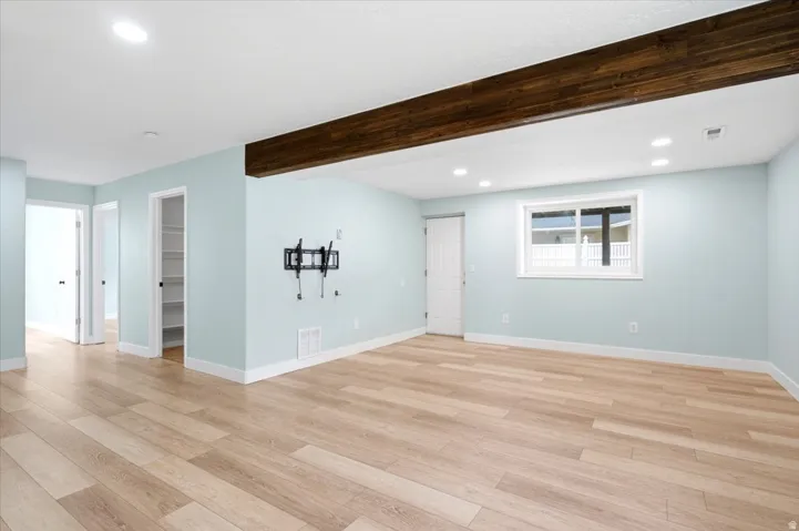 Spacious room featuring wood-finish flooring, recessed lighting, a prominent exposed wood beam, and a single window