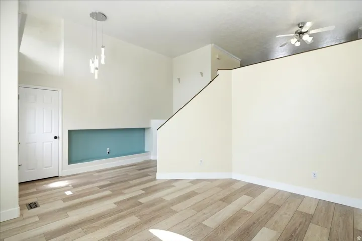 Vaulted ceiling, wood-finish flooring, built-in display nook, contemporary pendant lighting, and ceiling fan