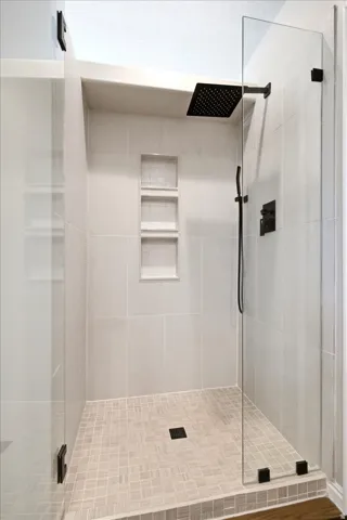 Glass-enclosed shower with a matte black square rain showerhead, coordinated handheld sprayer, and built-in recessed shelving