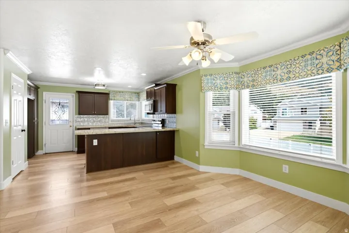 Wood-finish flooring, dark wood cabinetry, light-toned countertops, decorative tile backsplash, and a multi-panel bay window