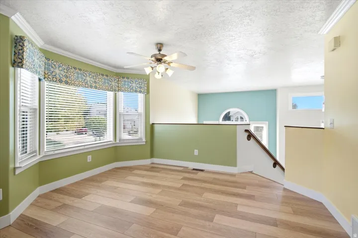 Wood-finish flooring, bay window with blinds, ceiling fan, accent wall with arched window, and staircase with wooden handrail