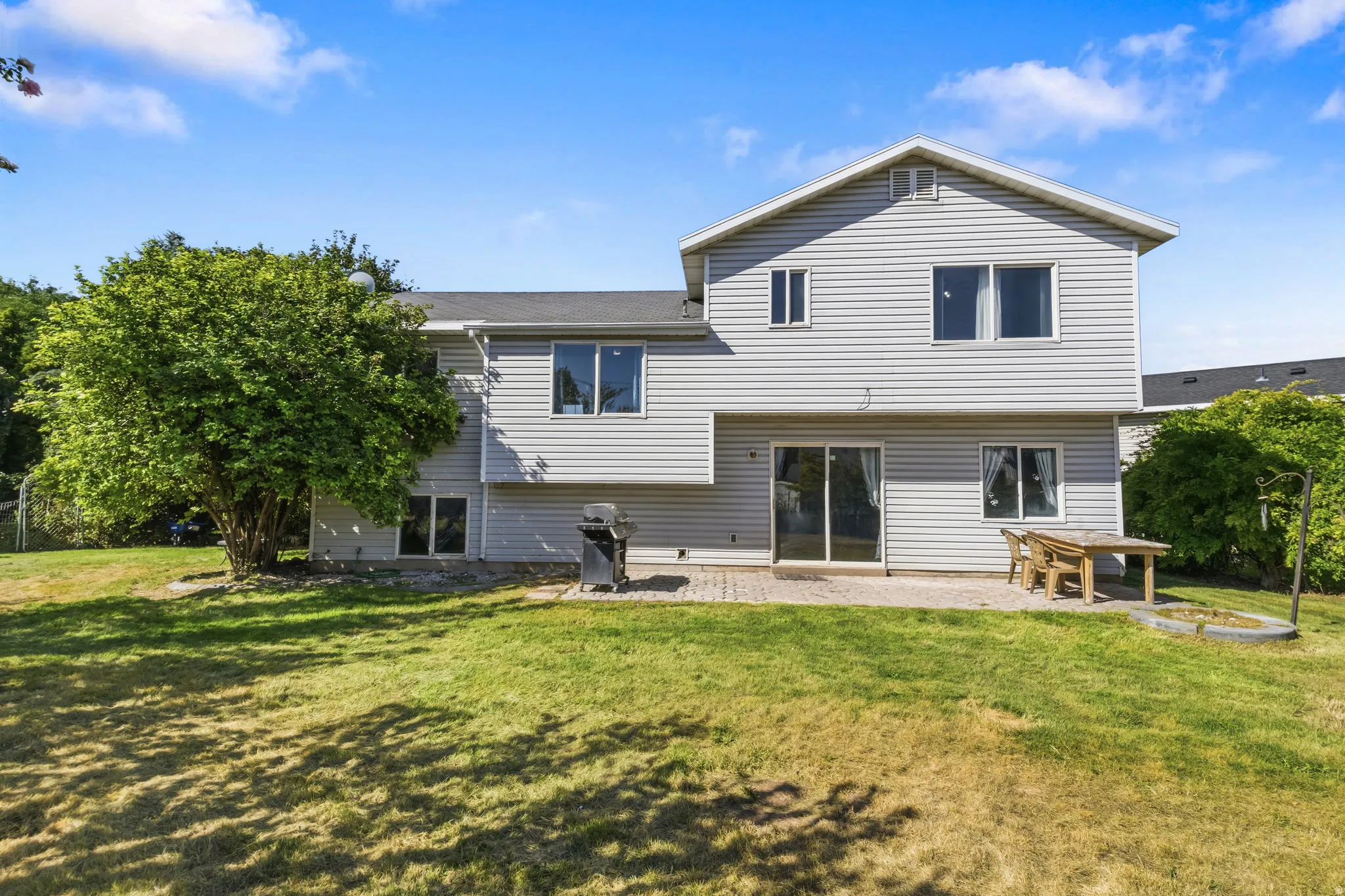 Expansive backyard with a manicured lawn, mature trees, and a paver patio