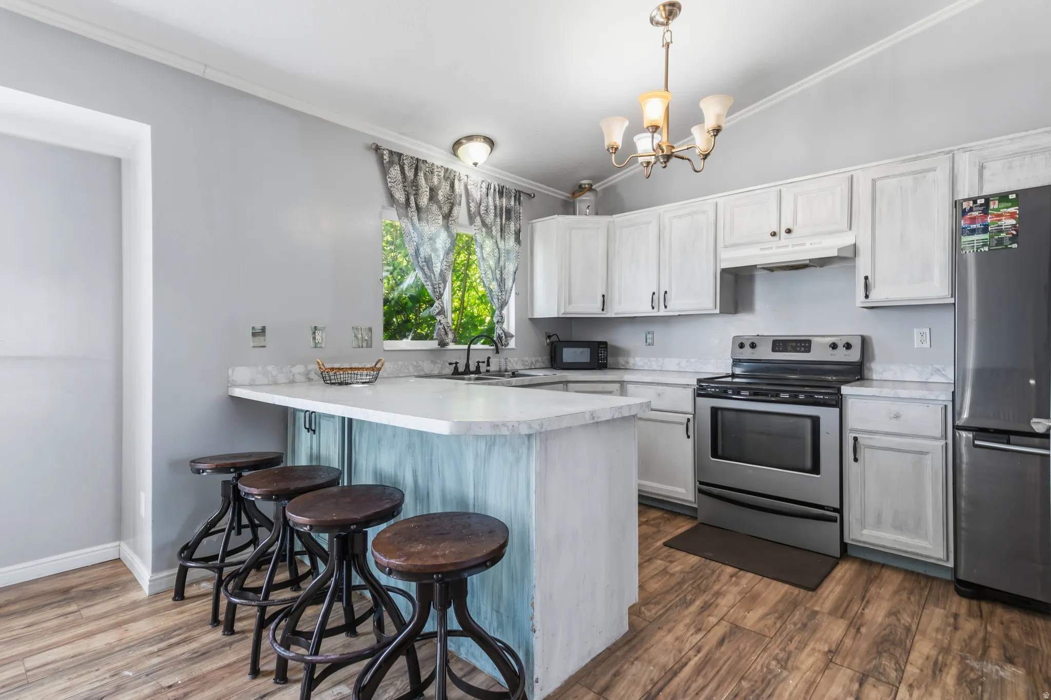 Vaulted ceiling kitchen featuring wood-finish flooring, white cabinetry, stainless steel appliances, and a breakfast bar with countertop