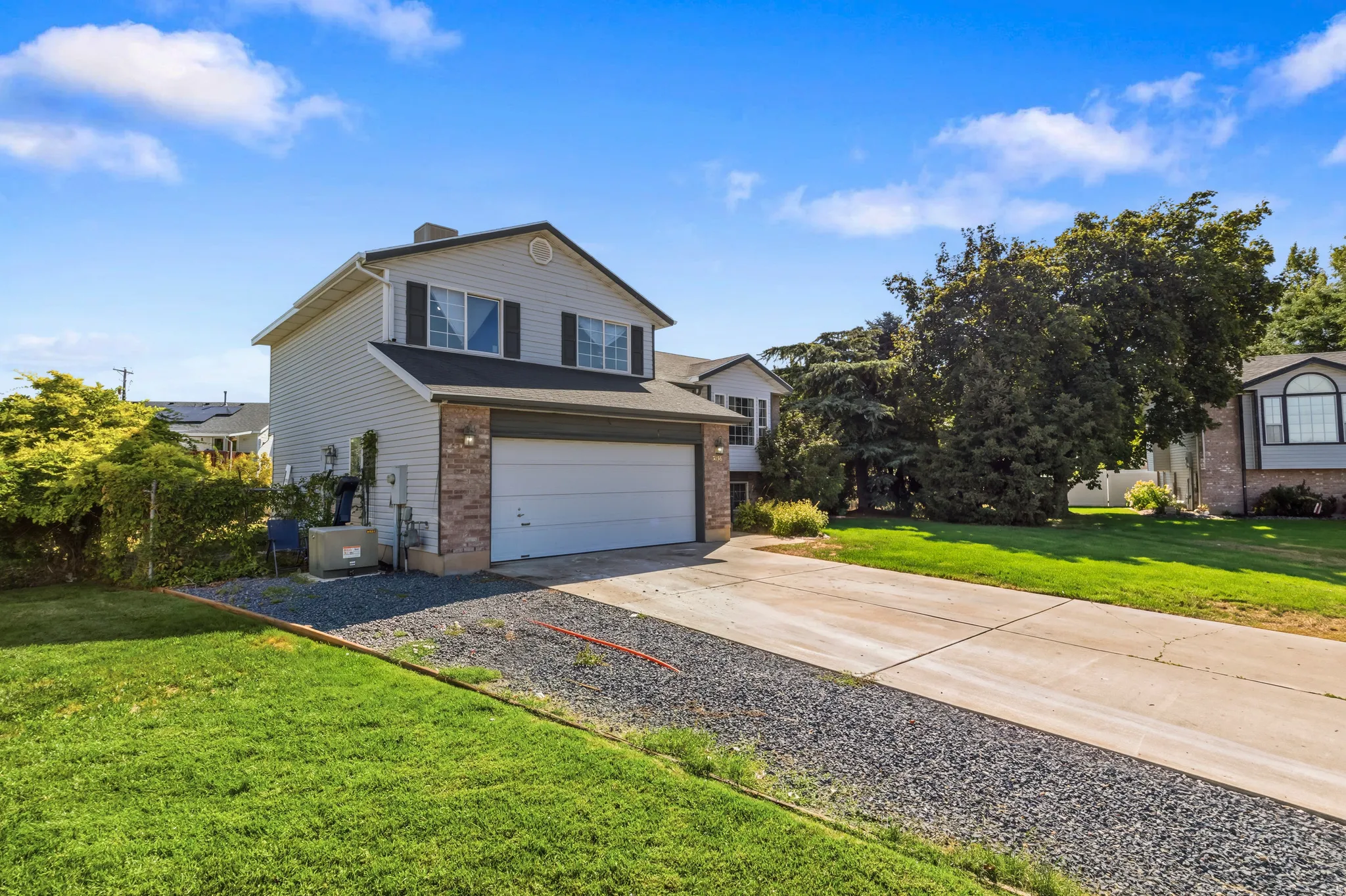 Two-story exterior with light gray siding, brick facade accents, a two-car garage, and a concrete driveway
