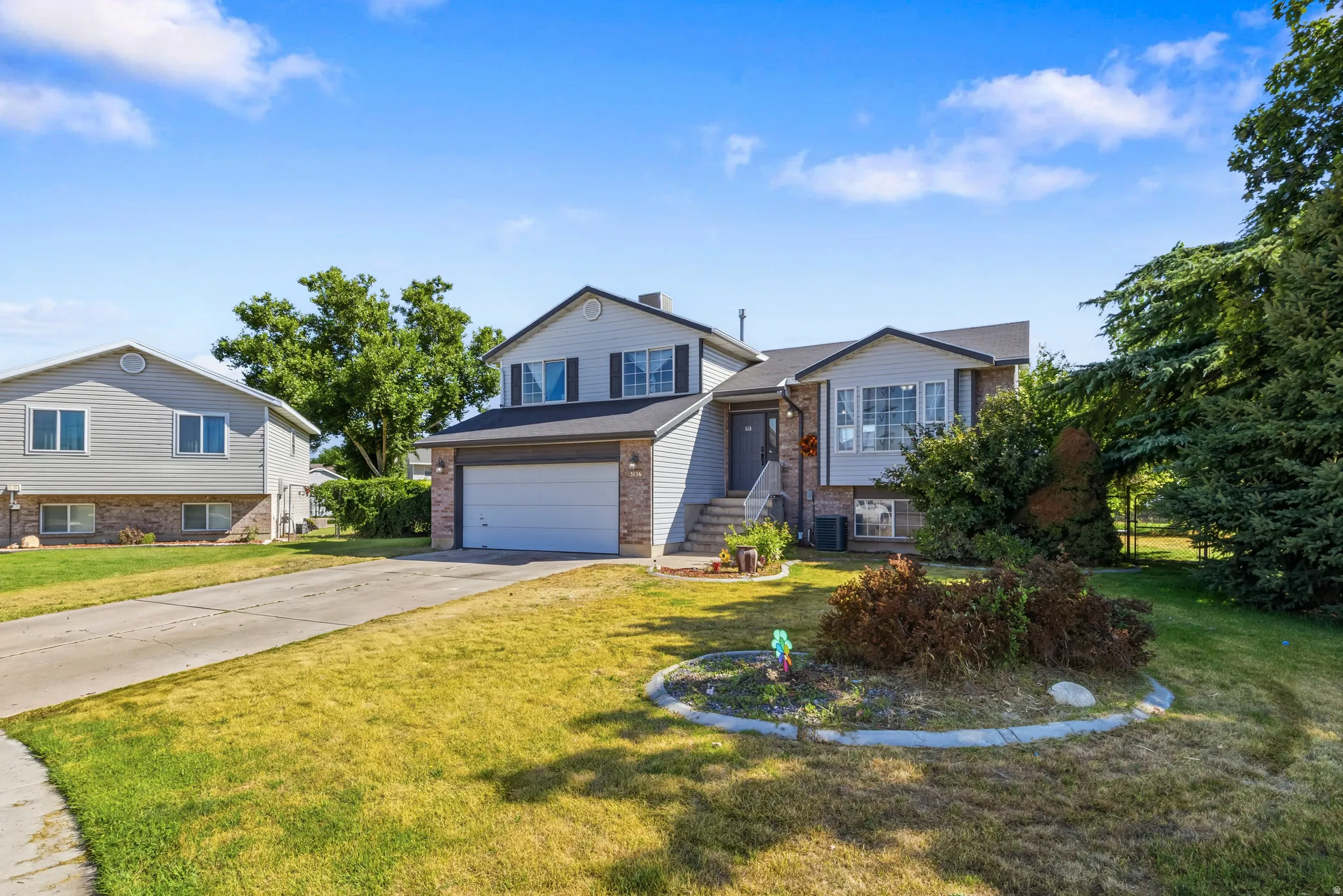 Split-level residence featuring a two-car garage, front yard landscaping, and mature trees