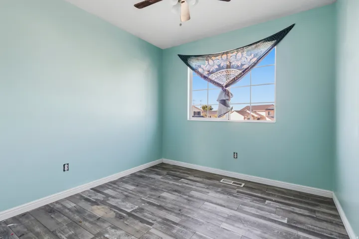 Window with grid panes, wood-finish flooring, ceiling fan with light fixture, and light blue wall color