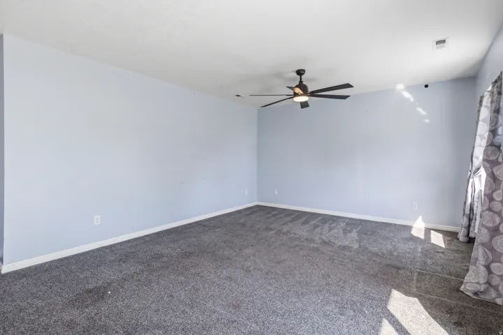Spacious room featuring light blue walls, gray carpet, and a ceiling fan with integrated lighting