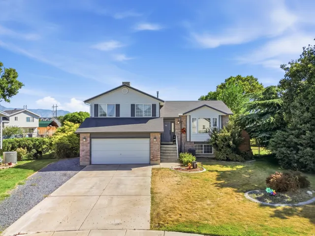 Split-level residence featuring a brick facade, attached two-car garage, concrete driveway, and established landscaping
