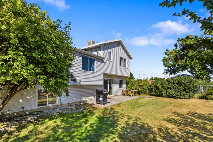 Expansive backyard featuring a concrete patio, sliding glass door access, and mature trees