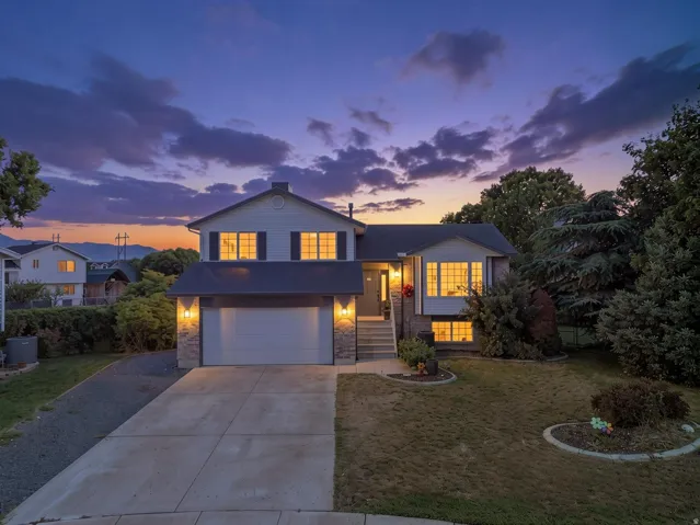 Two-story residence featuring a two-car garage, stone and siding exterior, concrete driveway, and mature landscaping
