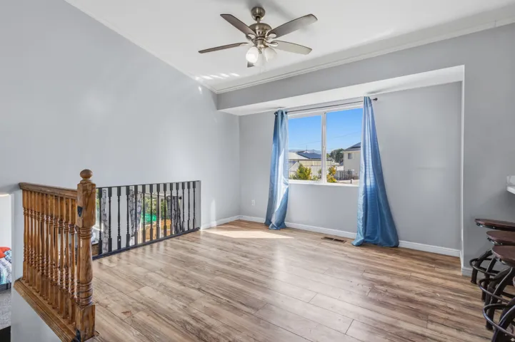 Spacious room featuring wood-finish flooring, a contemporary ceiling fan, and a large window with ample natural light