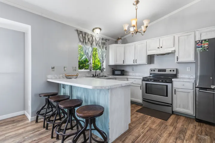 Vaulted ceiling kitchen featuring wood-finish flooring, white cabinetry, stainless steel appliances, and a breakfast bar with countertop
