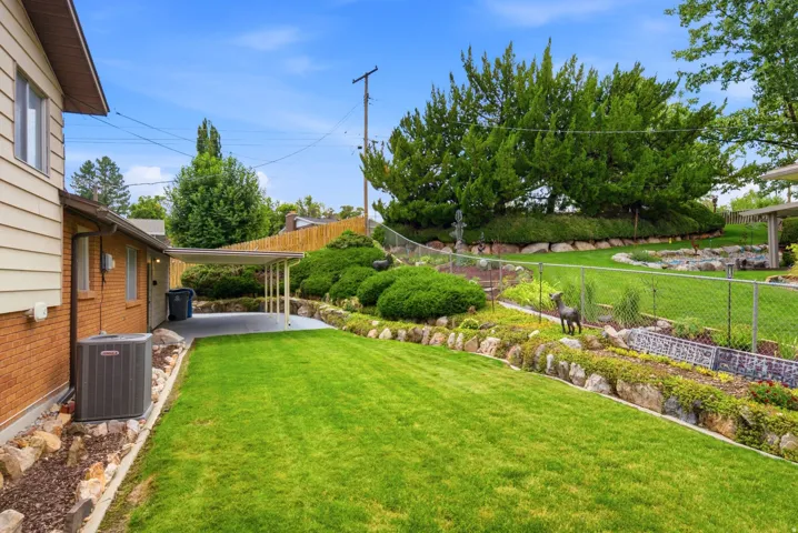 Expansive backyard featuring a manicured lawn, mature landscaping with mixed plantings, a retaining wall, stone edging and beautiful yard art