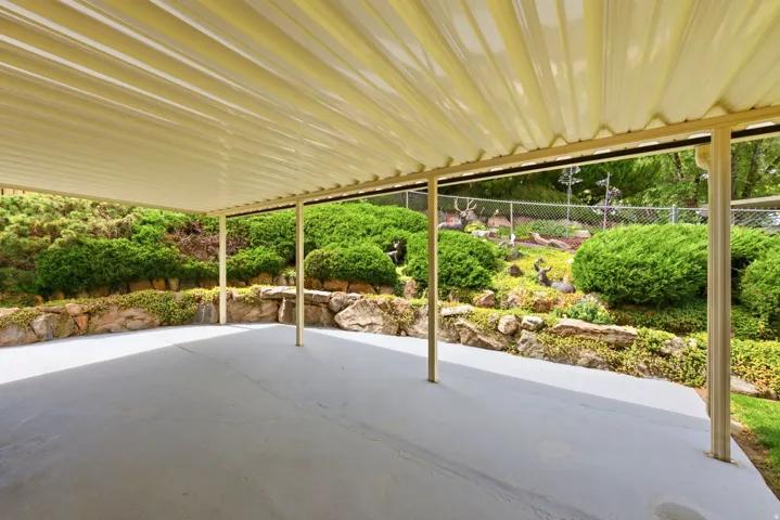 Expansive covered patio looking to the southeast, featuring a solid roof, support posts, concrete flooring, and an elevated rock garden with established shrubs and yard art