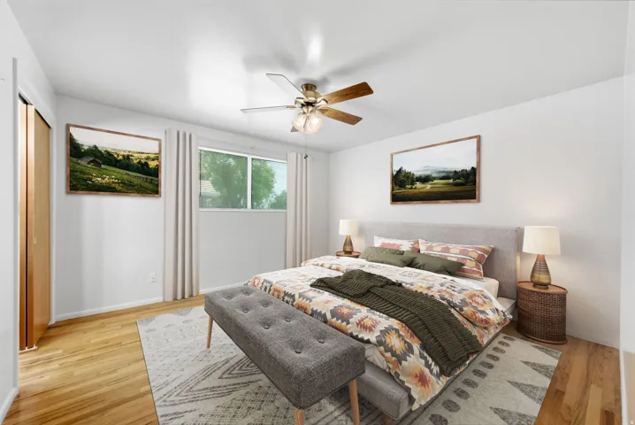 Upper level primary bedroom virtually staged to show possibilities with hardwood flooring, ceiling fan, and window with natural light