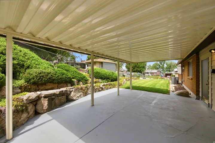 Expansive covered patio looking to the southwest, featuring a solid roof, support columns, concrete flooring, and support posts