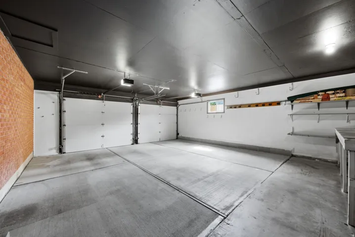 Spacious attached garage with two overhead insulated doors, concrete flooring, exposed brick wall, built-in shelving, and window