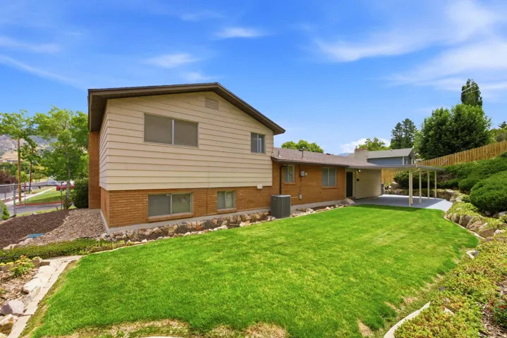Expansive backyard featuring a green lawn, integrated rock landscaping, and a covered patio