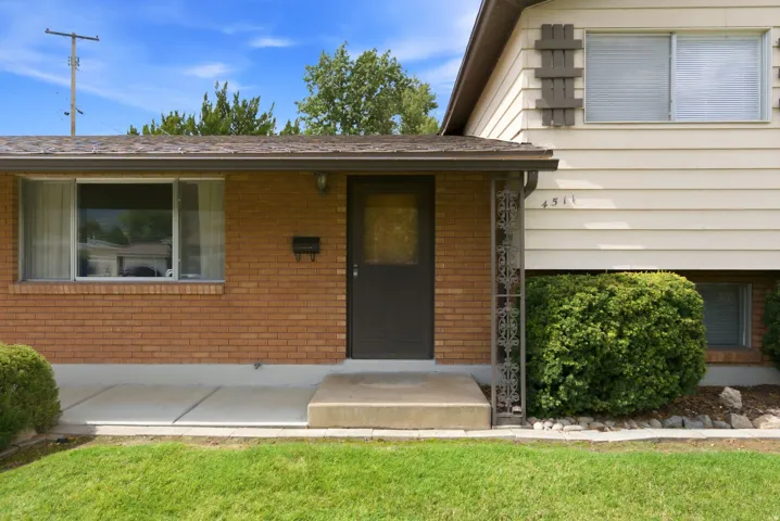 Front of home with brick exterior with siding accents, covered entry, front door, and mature landscaping