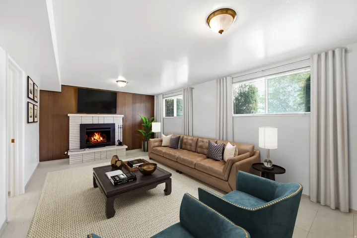 Lower level family room virtually staged to show possibilities featuring a white brick fireplace, wood paneling, multiple windows, and overhead lighting