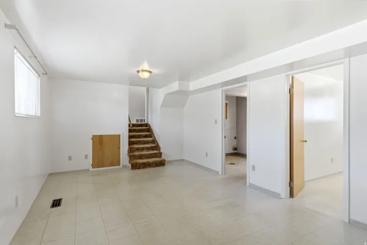 Lower level family room featuring vinyl tile flooring, stairs to main level, access door to laundry room/storage/furnace areas, access door to basement bedroom, and access door to the crawl space