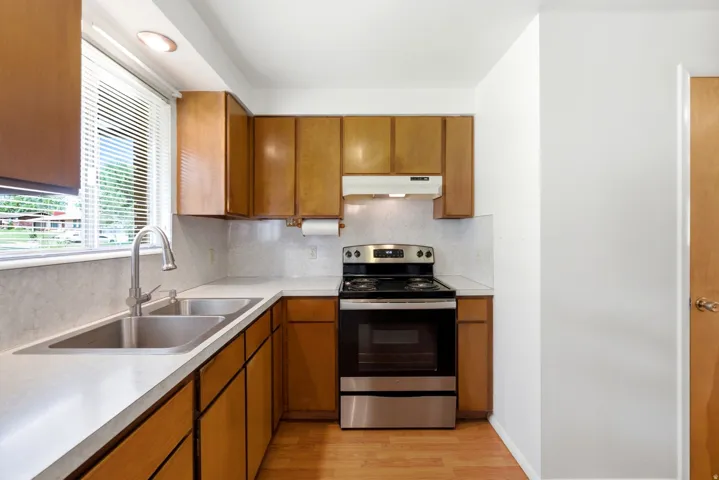 Main level kitchen featuring wood cabinetry, vinyl (LVP) flooring, light-toned countertops, dual basin stainless steel sink, and free-standing electric oven/stove