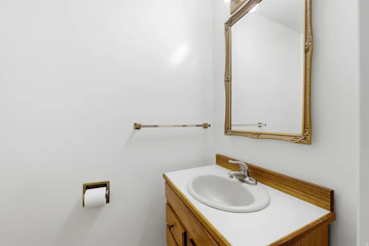 Main level hall half-bathroom with vanity, wood cabinetry, white countertop, and integrated sink