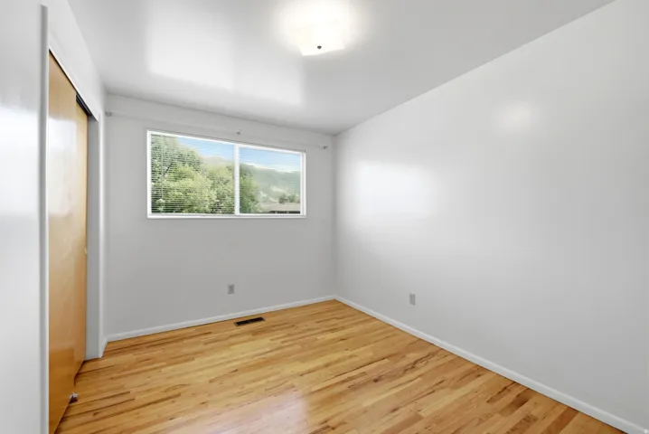 Upper level bedroom with hardwood flooring, white walls, flush mounted lighting, sliding window, and closet with built-in shelves and sliding doors
