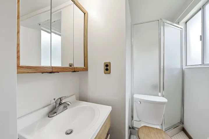 Upper level primary three-quarter bathroom with white vanity with integrated sink, chrome-finish faucet, framed medicine cabinet, and enclosed shower stall