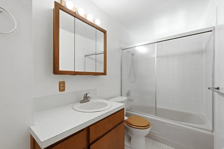 Upper lever hall full-bathroom with white vanity with integrated sink, wood cabinetry, and a mirrored medicine cabinet