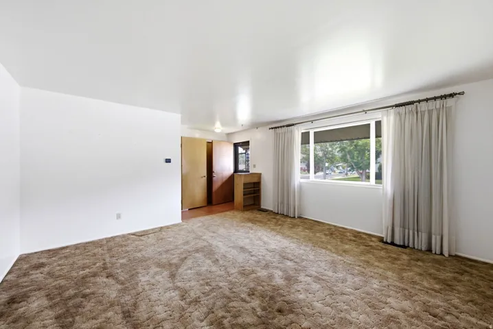 Spacious front living room with neutral carpeting, white walls, and a large window