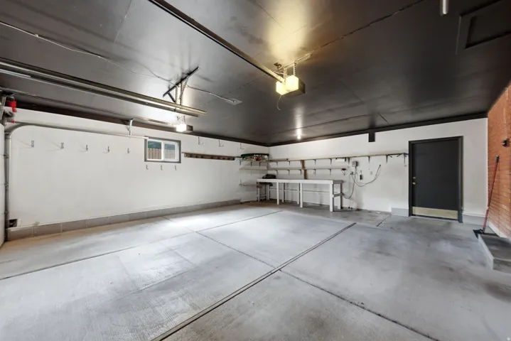Spacious garage with concrete flooring, painted walls, storage shelving, workbench, and door access to the rear yard