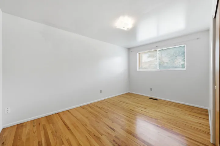 Upper level bedroom two with hardwood flooring, white walls, flush mount lighting, sliding window, and closet with built-in shelves and sliding doors