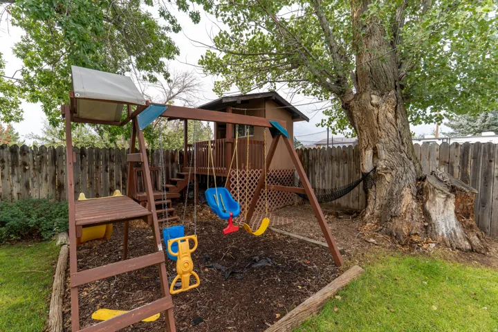 Wood privacy fencing, mature trees, wooden play structure, grassy area, mulched ground cover
