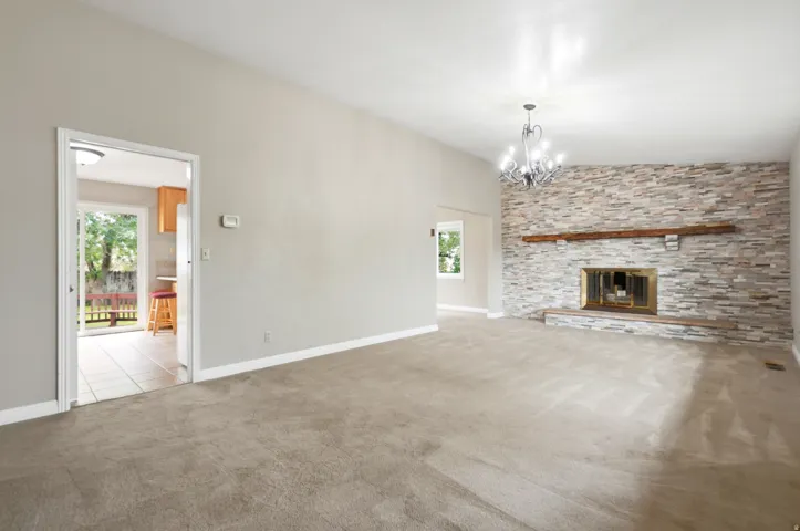 Carpeted living area featuring a stone accent wall, fireplace with a wood-finish mantel, and a multi-arm chandelier