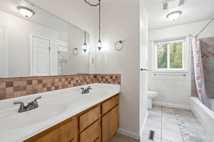 Dual vanity with wood-finish cabinetry, a full-width mirror, and tile backsplash