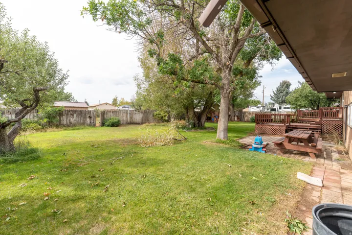 Expansive backyard featuring a tiered wood deck, mature trees, a brick paver patio, and a wood fence