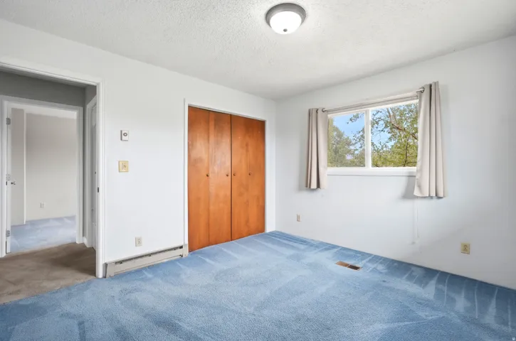 Spacious bedroom featuring hardwood closet doors, neutral wall finishes, and abundant natural light from a large window with exterior views