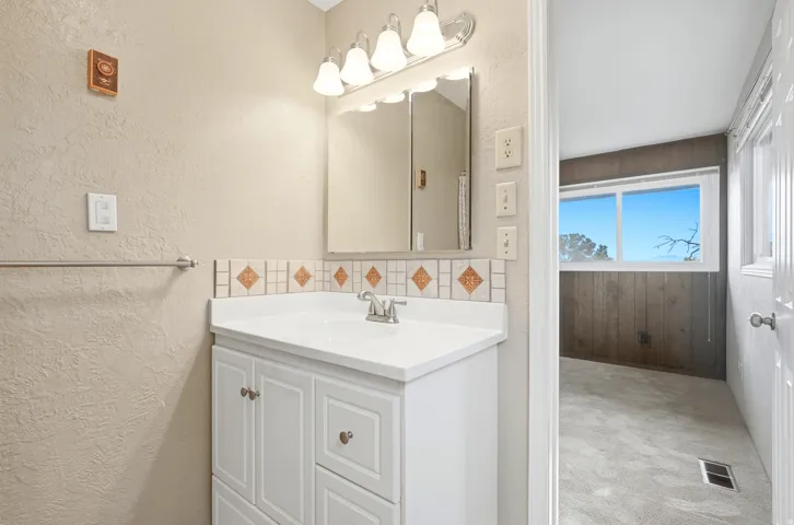 White vanity with cabinet storage, integrated sink, and decorative tiled backsplash
