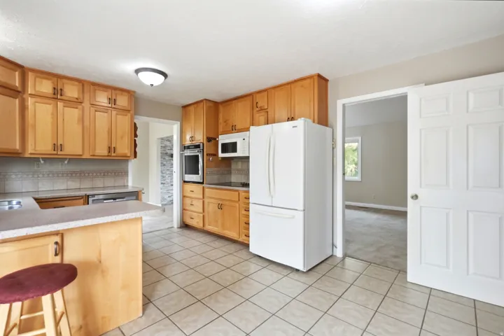 Kitchen featuring wood-finish cabinetry, white appliances, tile flooring, and a breakfast bar with solid surface countertop