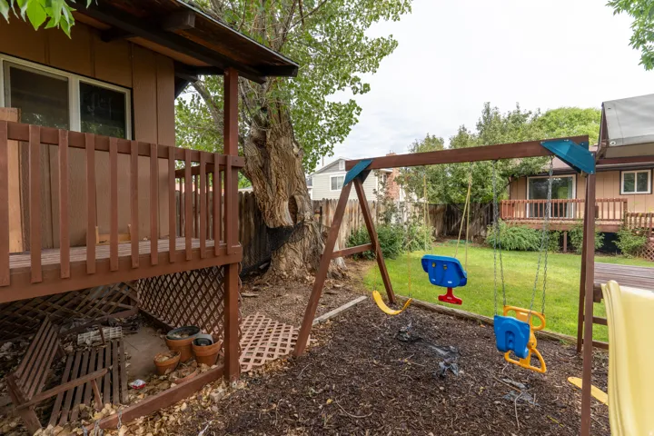 Rear yard featuring a wooden deck with railing, a mature tree, and a swing set over a mulched area