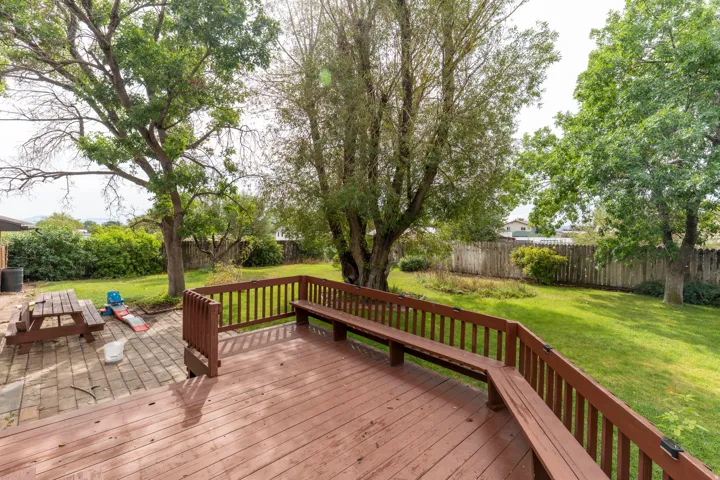 Spacious backyard featuring a wood deck with built-in bench seating, a stone paver patio, a manicured lawn, and mature trees