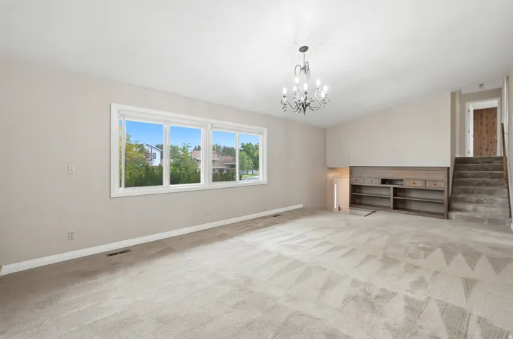 Spacious room featuring light-toned carpeting, a multi-pane window, a built-in shelving unit, and a chandelier