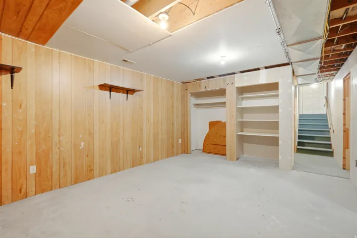Lower level featuring wood paneling, open ceiling joists, built-in shelving, and exposed ductwork